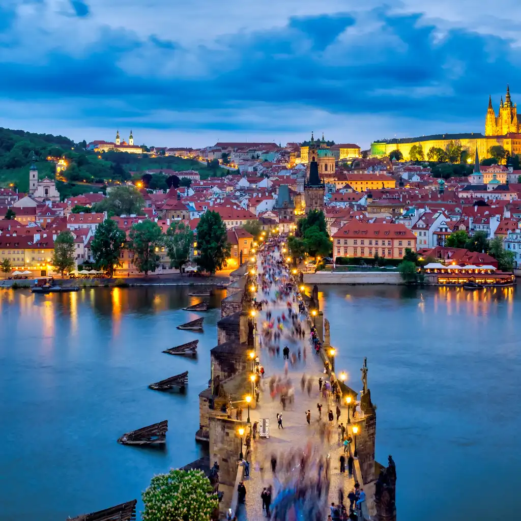 Charles Bridge Prague at dusk with blurred crowds, glowing lights and Prague Castle view
