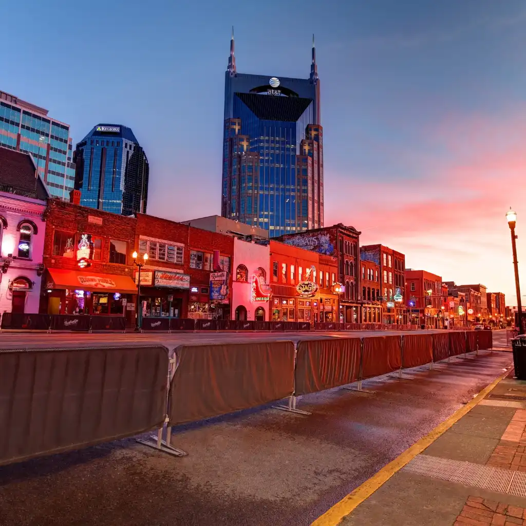 Lower Broadway Nashville bars glowing at dusk with AT&T Building skyline and street barricades