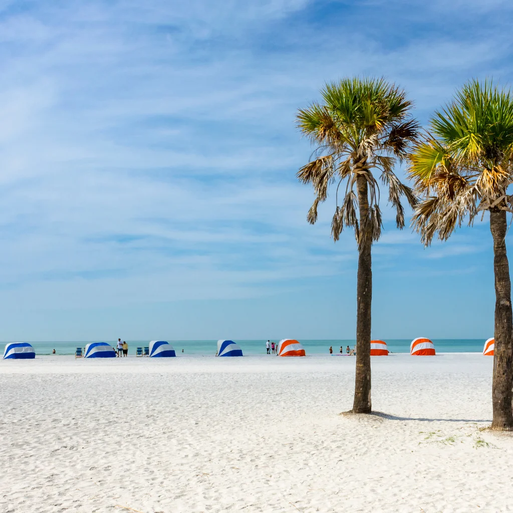 Clearwater Beach Florida white sand beach with palm trees and blue orange striped tents by calm sea