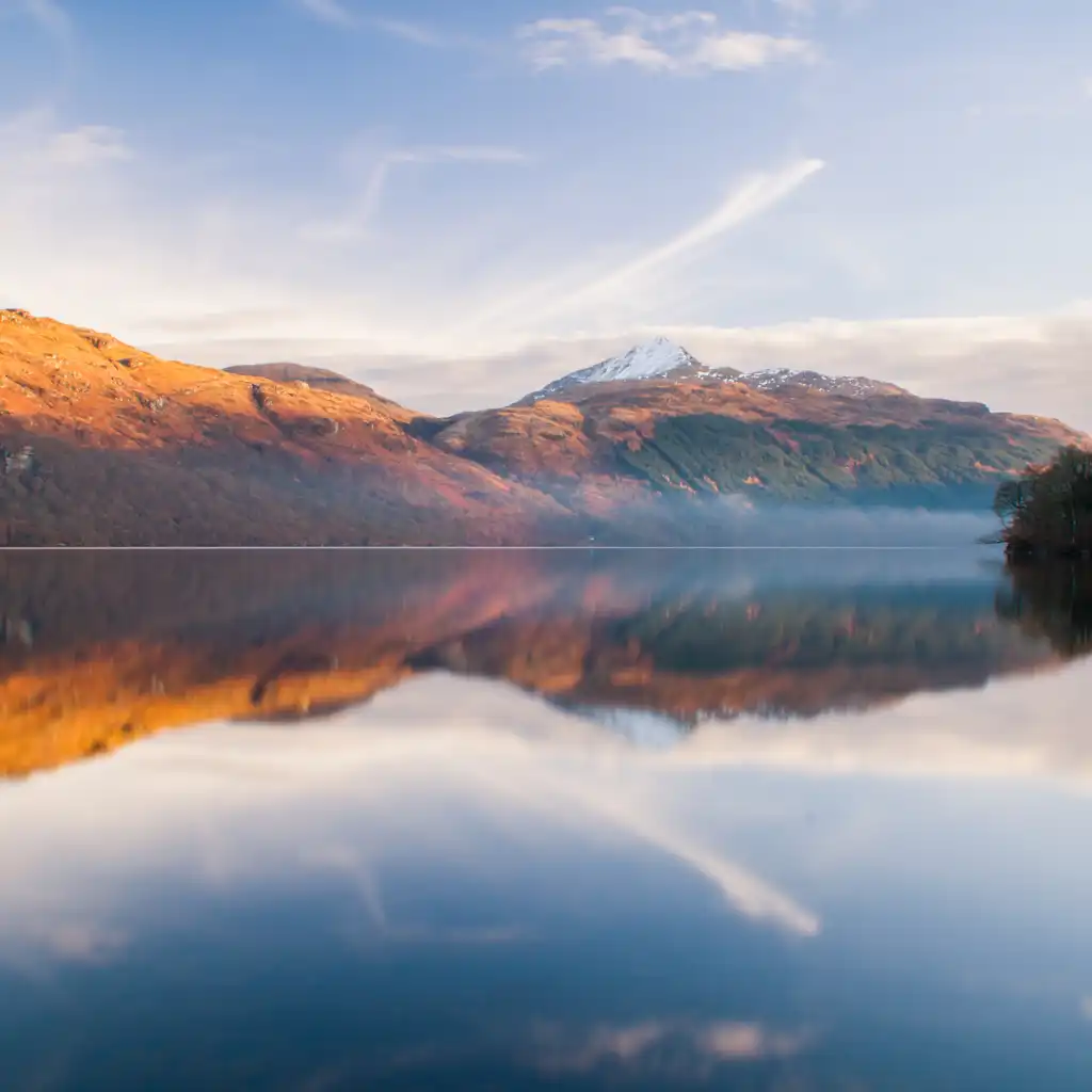 Loch Lomond Scotland calm waters reflecting autumn mountains with snow peak and mist