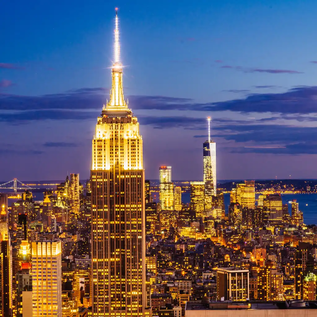 Empire State Building New York glowing at night in illuminated city skyline with One World Trade Center