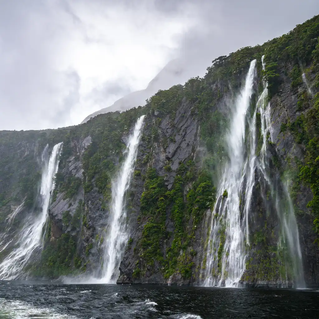 Milford Sound waterfalls cascading down lush cliffs into dark waters near Queenstown New Zealand