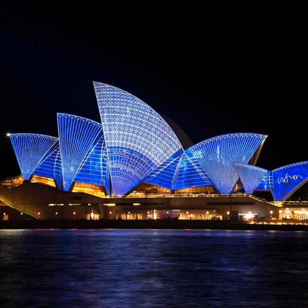 Opera House Sydney glowing blue at night over the harbor water