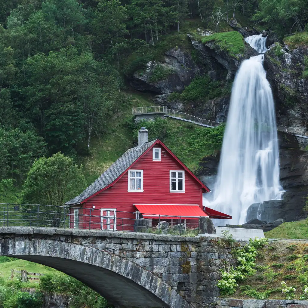 Steinsdalsfossen waterfall behind red house and stone bridge in Hardanger Norway