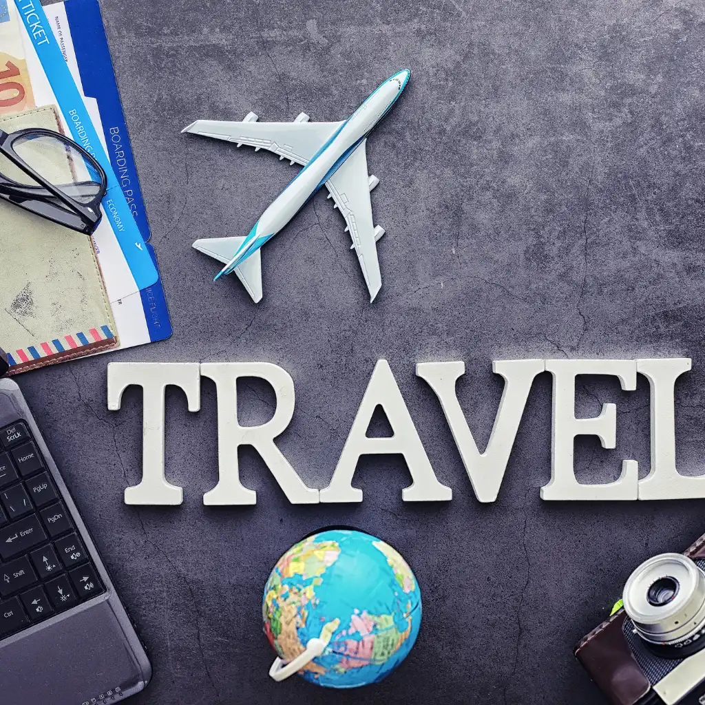 Travel booking flat lay with toy airplane, globe, passport, tickets and TRAVEL letters