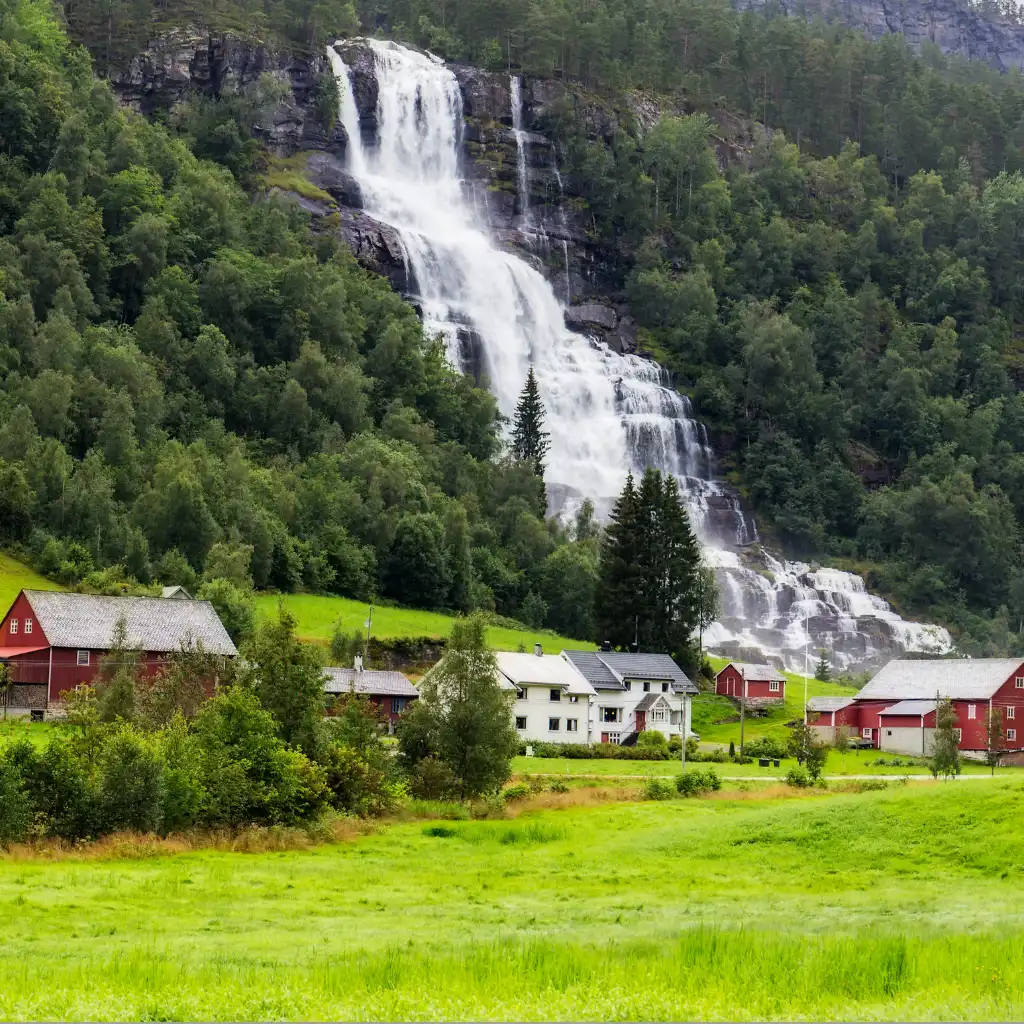 Tvindefossen waterfall cascading over cliffs near red houses and fields in Voss Norway