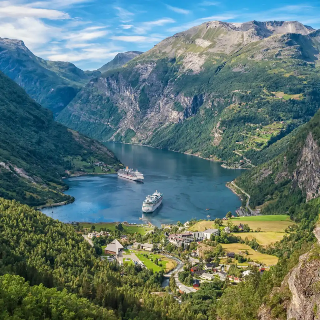 Geiranger, Norway fjord with cruise ships amid steep green mountains and village below
