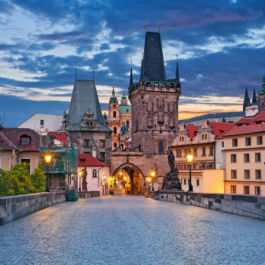Prague, Czechia Charles Bridge tower at dusk with cobblestone path and lanterns