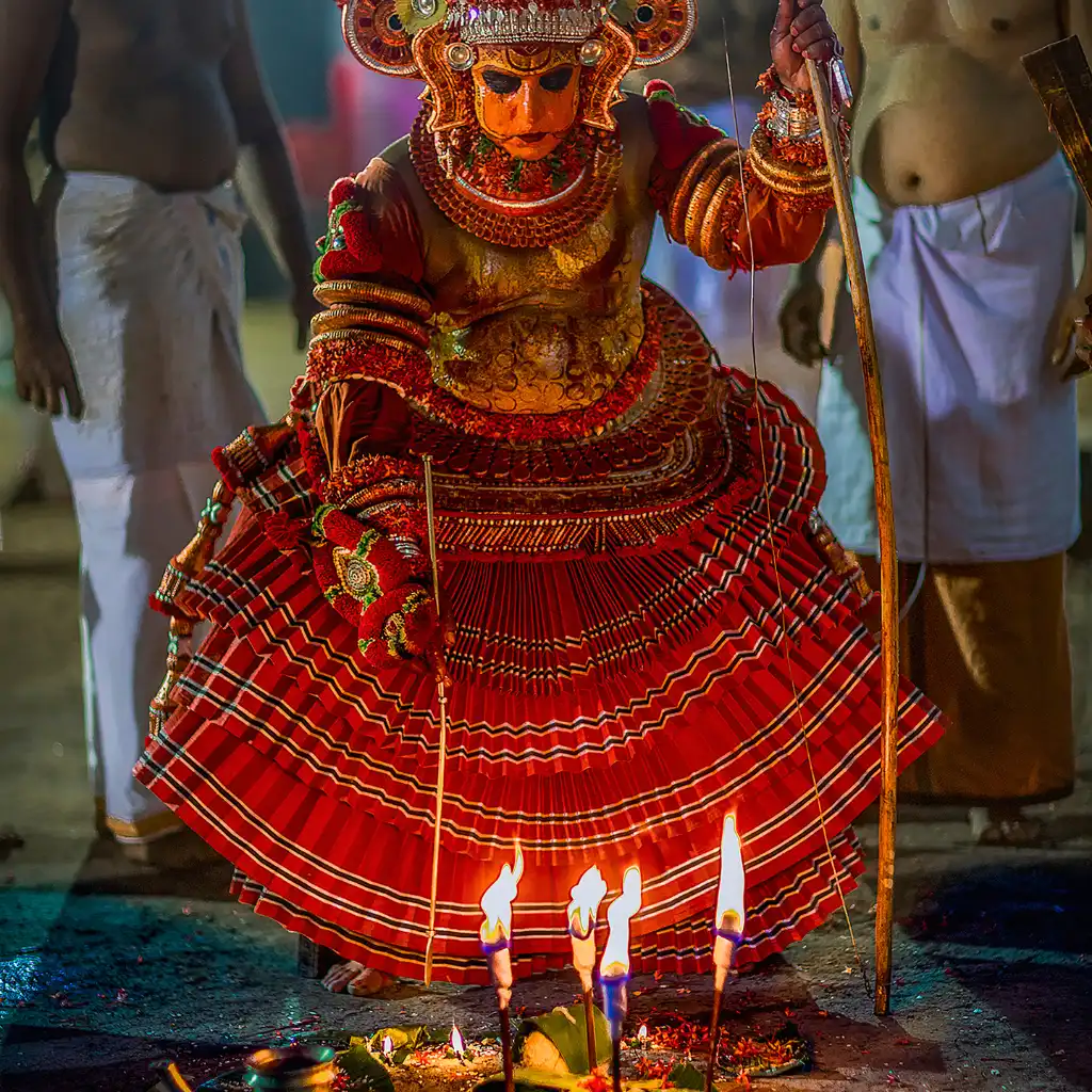 Theyyam ritual performer in ornate red costume with lit lamps in Kannur, Kerala