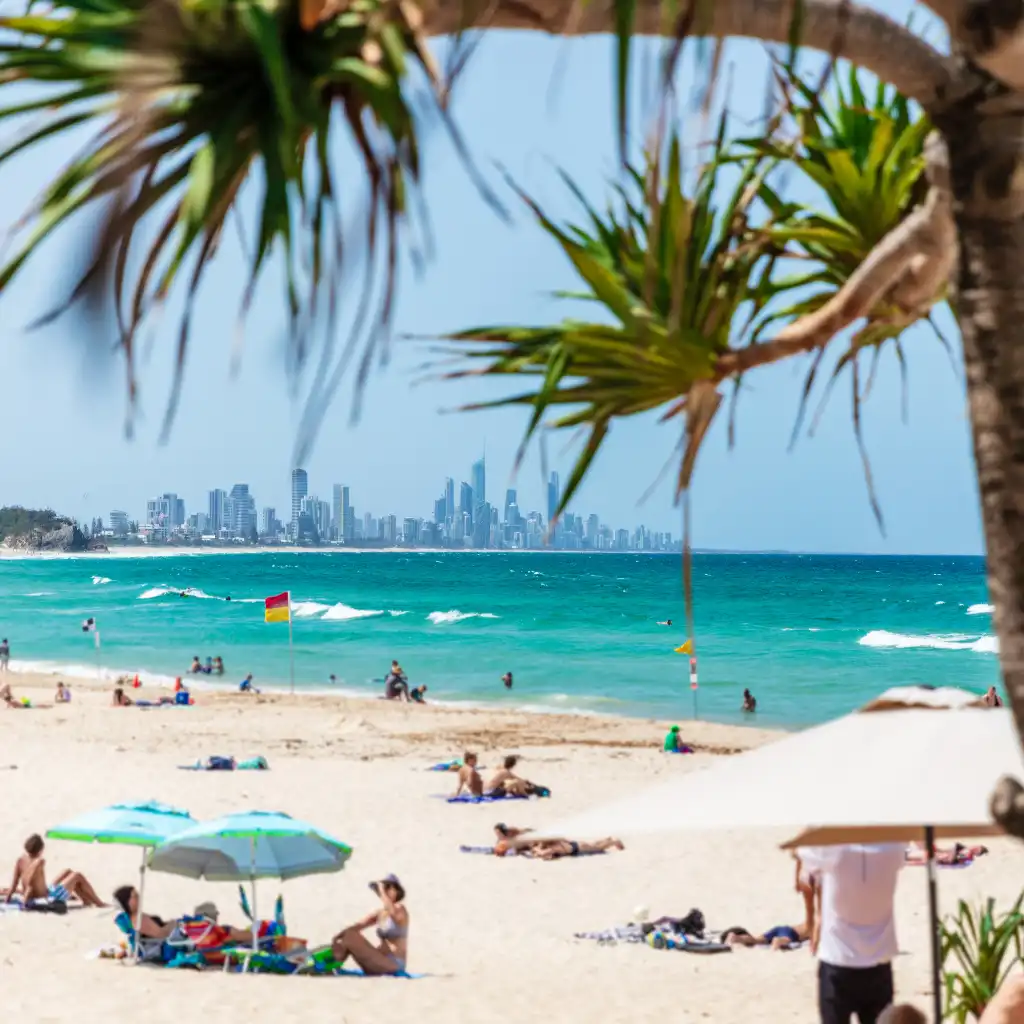 Burleigh Beach Gold Coast with sunbathers, umbrellas and skyline across turquoise waves