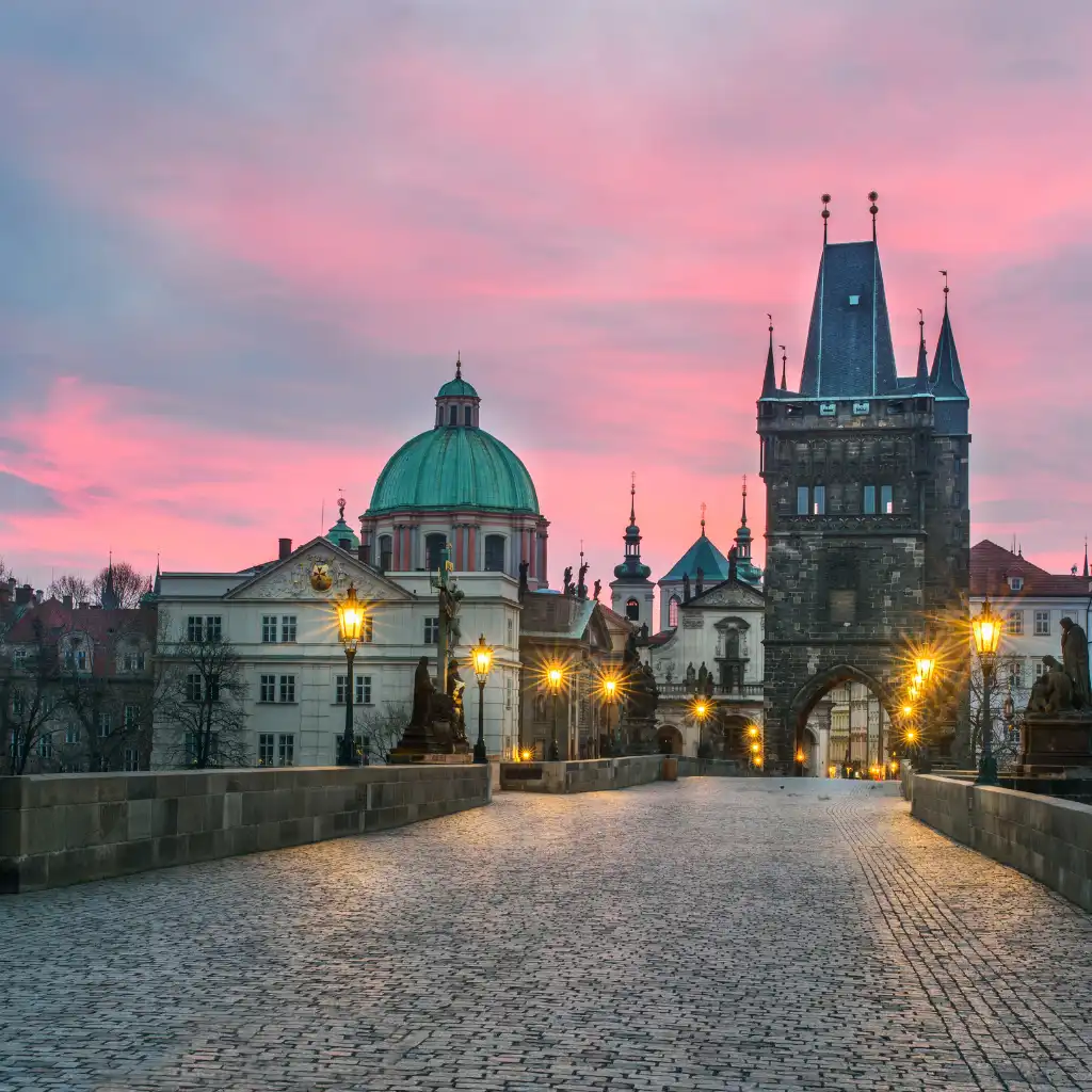 Charles Bridge Prague empty at dawn with pink sky glowing lamps and cobblestone path