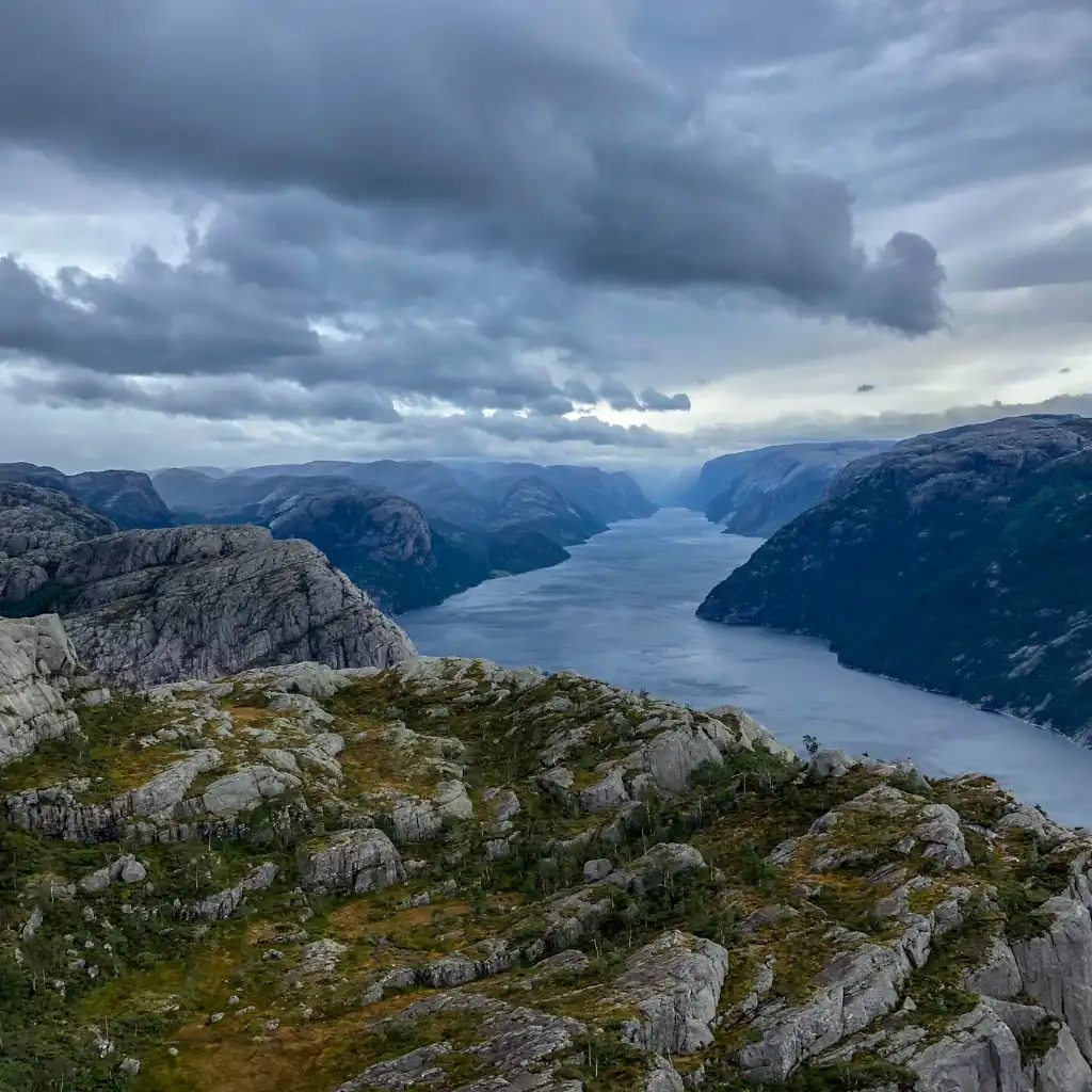 Preikestolen Norway rocky cliff hike overlooking fjord under dramatic clouds