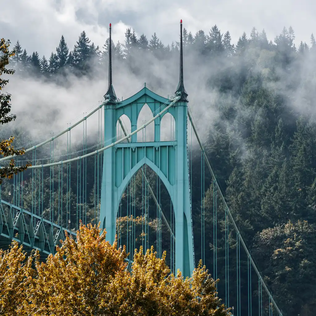 St Johns Bridge Portland towers piercing mist over lush forest with golden autumn foliage in foreground