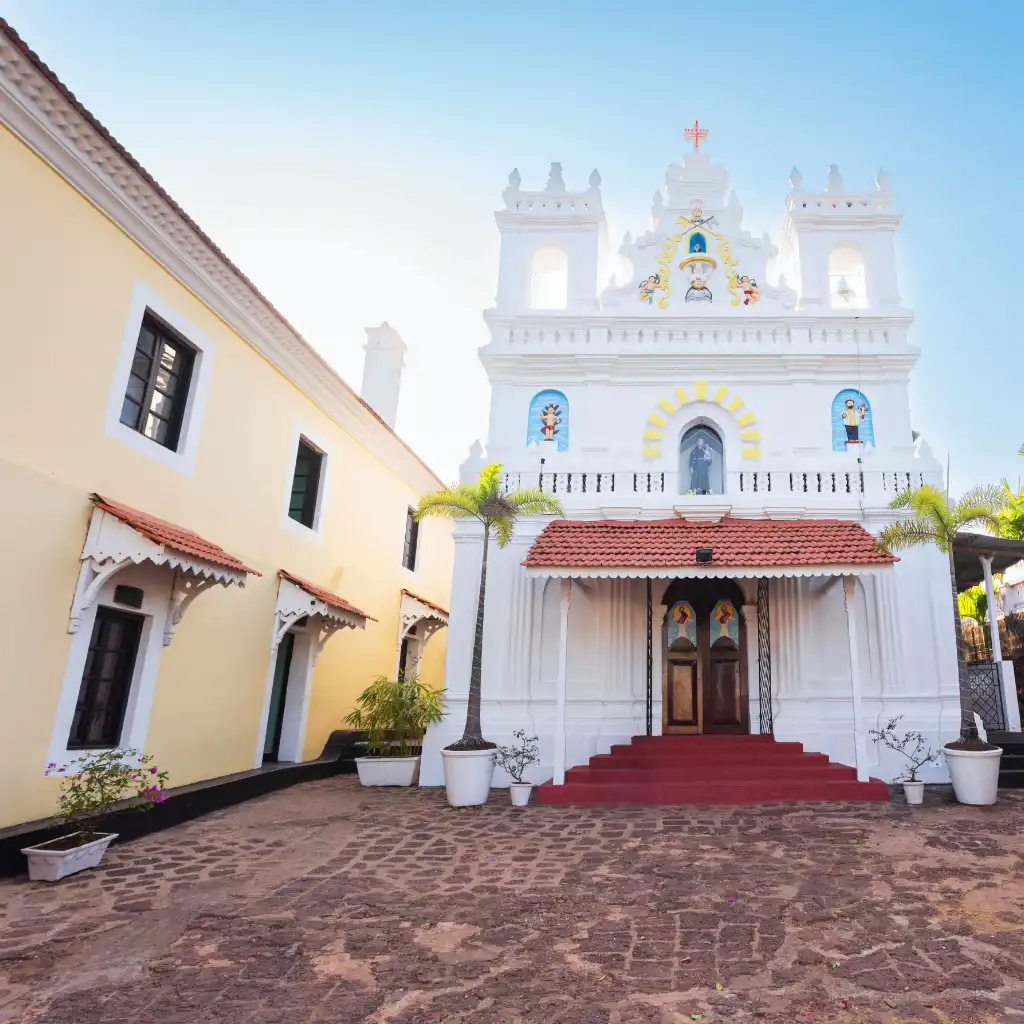 Terekhol Fort Goa white church facade with red steps, palm trees and cobblestone courtyard