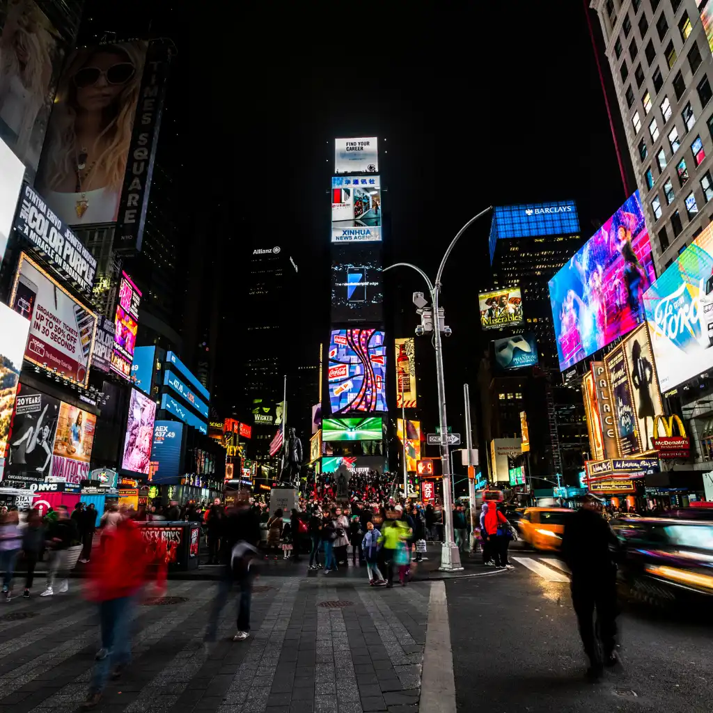 Times Square New York at night with crowds neon billboards and taxis near subway lines