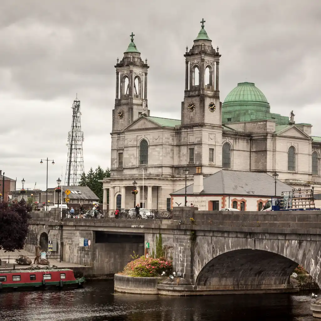 Overcast skies above Irish cathedral towers and green dome by river bridge with boats