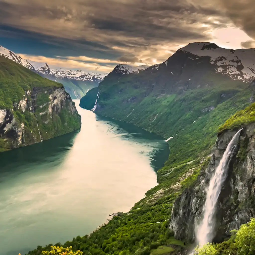 Geiranger Fjord Norway with cascading waterfall, steep green mountains and winding fjord waters