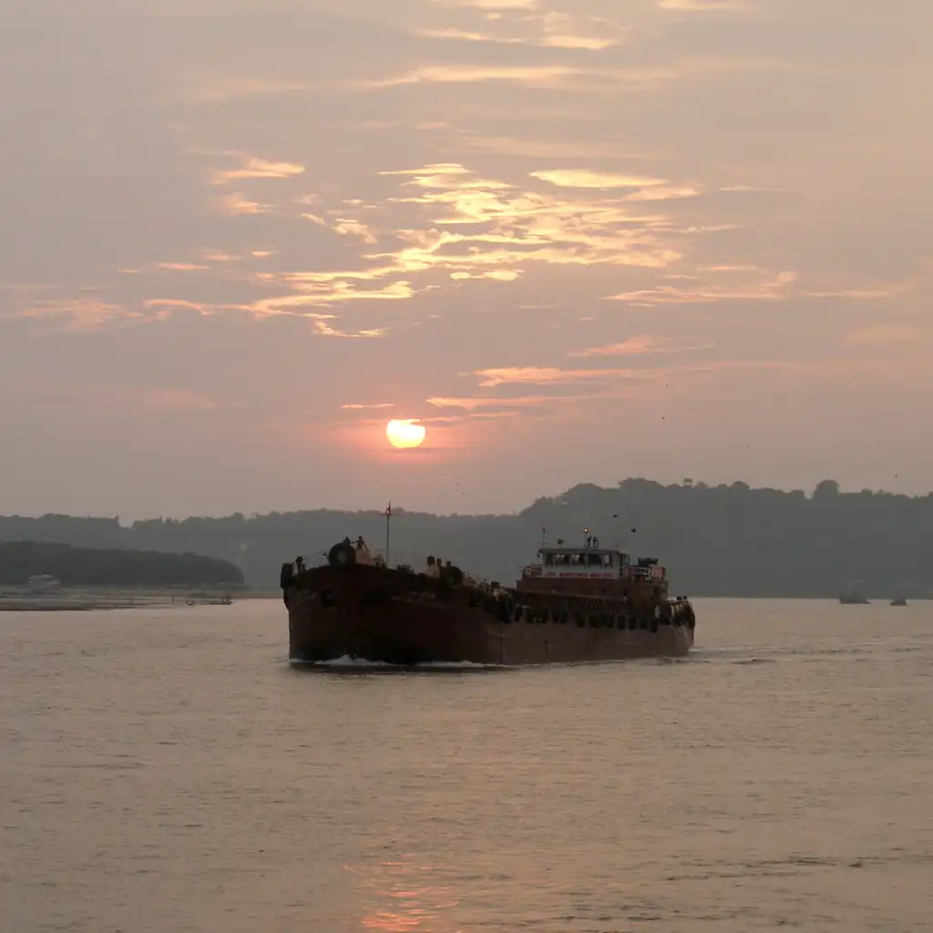 Cargo ship on Mandovi River at Sunset, Goa with golden sky and hills