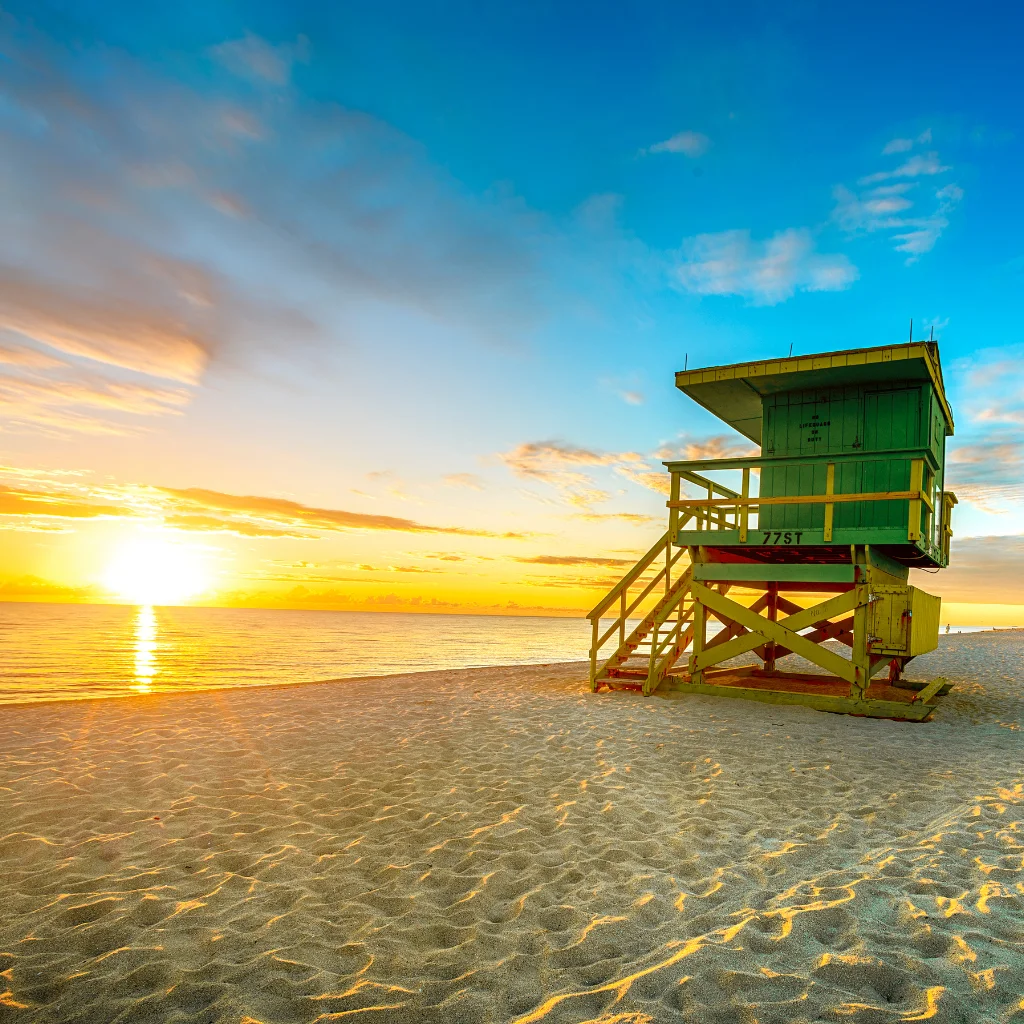 Miami Beach lifeguard tower at sunset with golden light reflecting on sand and ocean