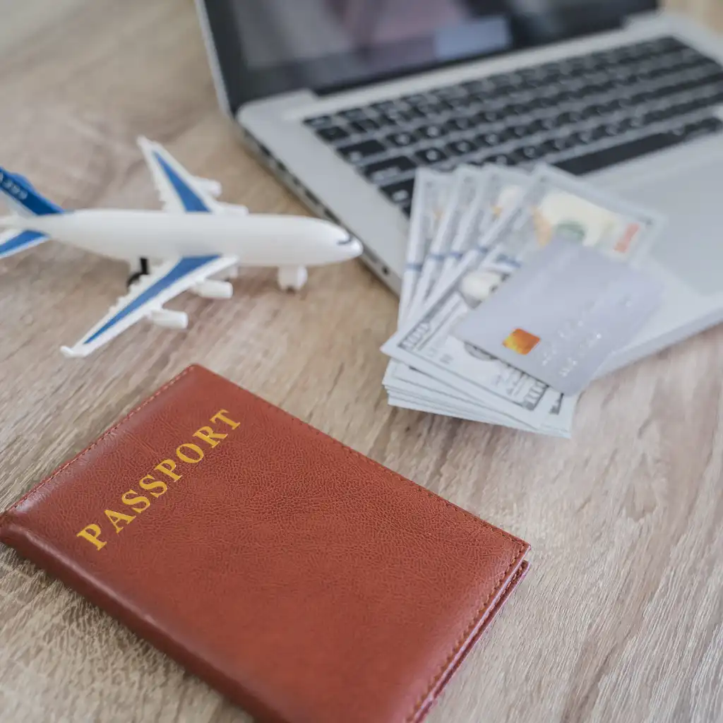 Perth travel booking essentials with passport, toy plane, laptop, cash and cards on wood table
