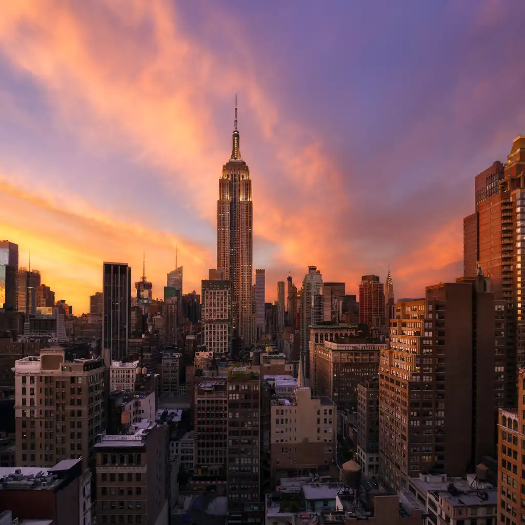 Manhattan New York sunset skyline with illuminated Empire State Building over city rooftops