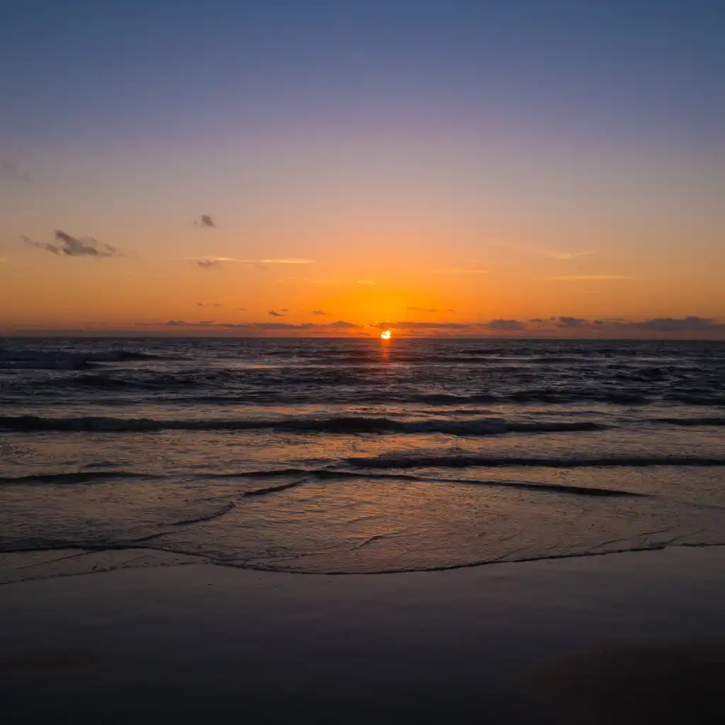 Sunset at Ashwem Beach Goa with golden sun over the ocean and waves on wet sand