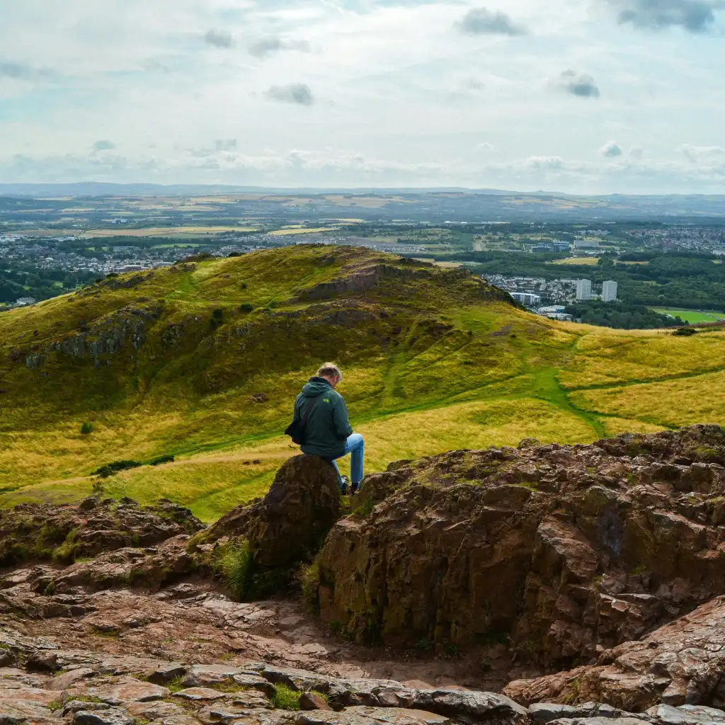 Hiker on dry rocks at Arthur's Seat Scotland with panoramic city views