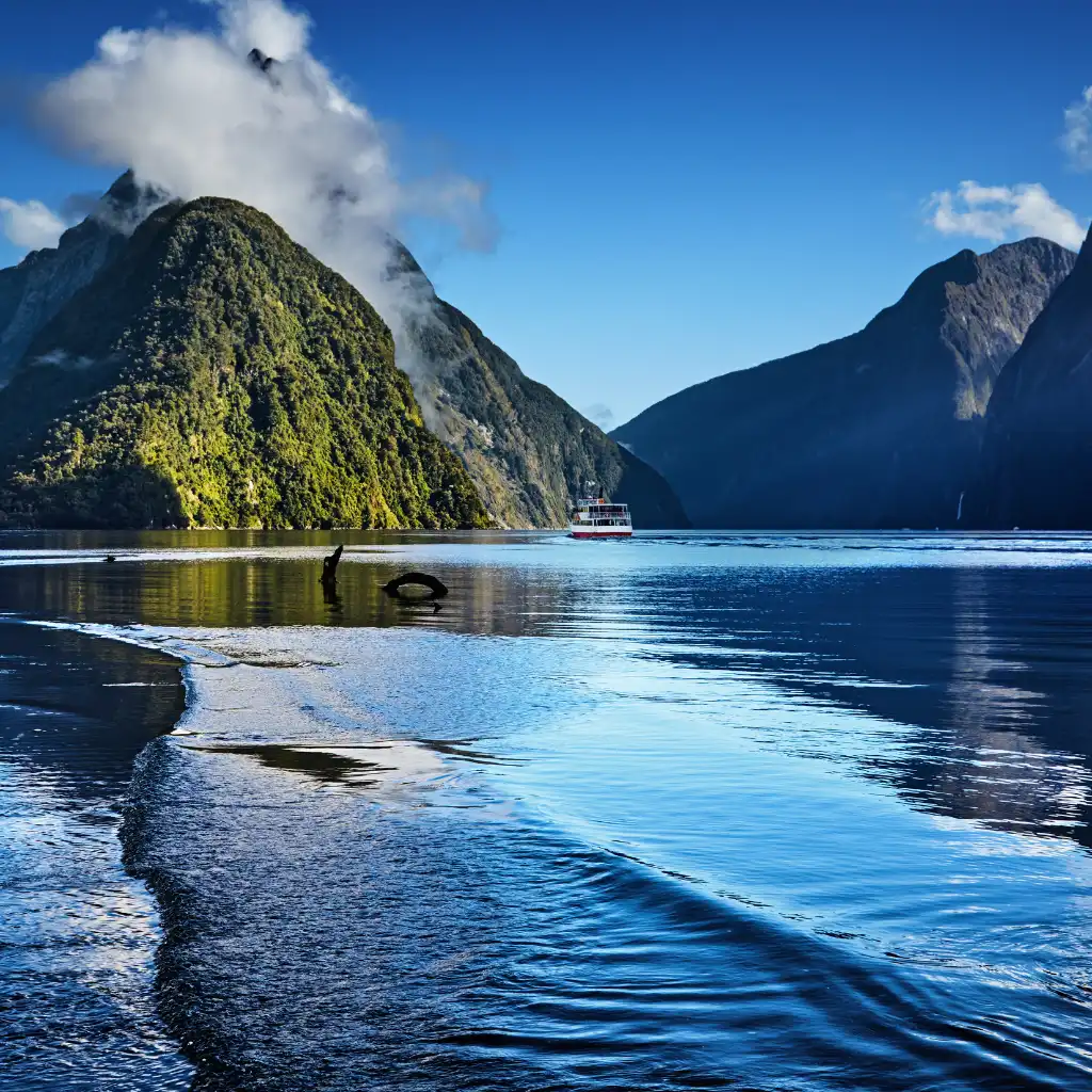 Milford Sound cruise boat amid misty mountains and glassy reflections near Queenstown, New Zealand