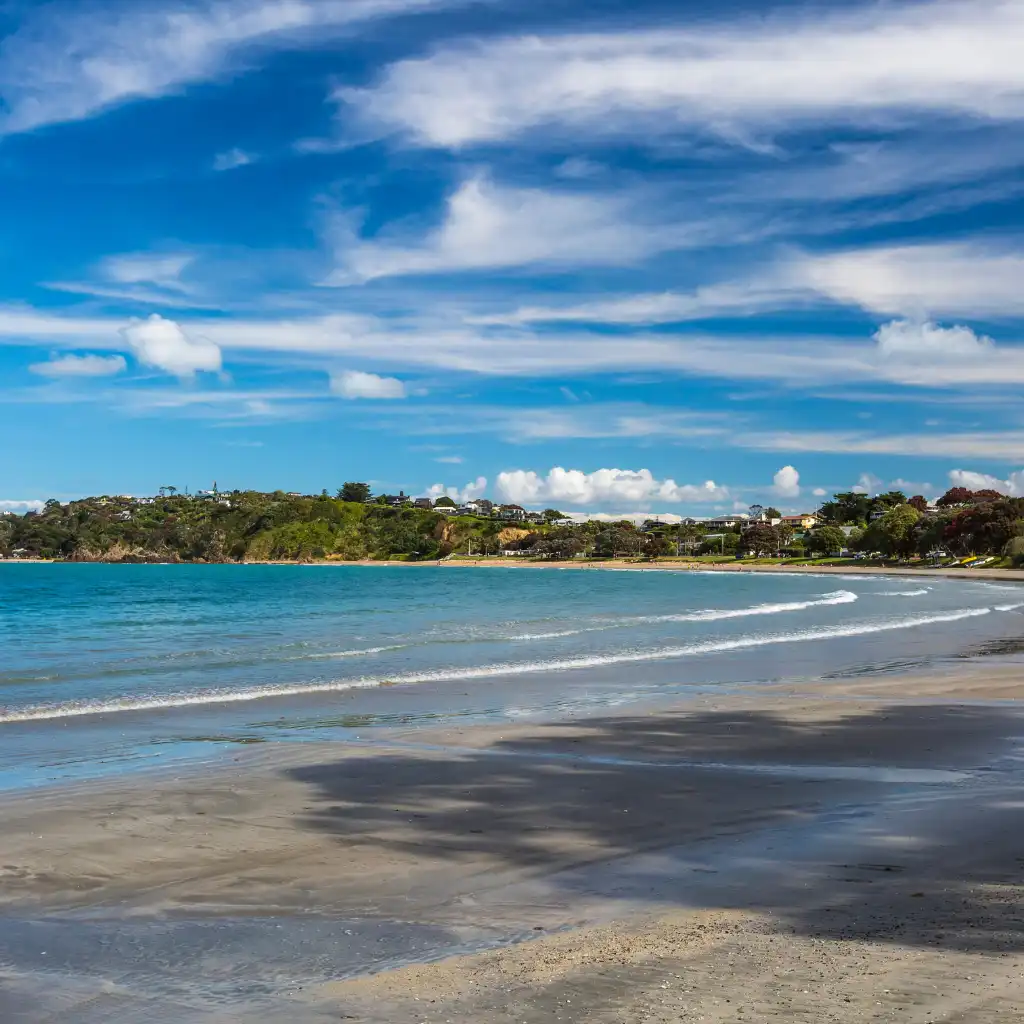 Waiheke Island Auckland bay beach with turquoise water gentle waves and green hillside homes