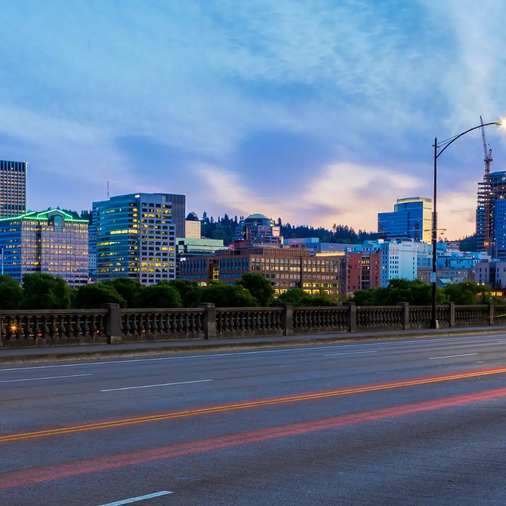 Burnside Portland skyline at dusk with glowing buildings and light trails on the bridge road