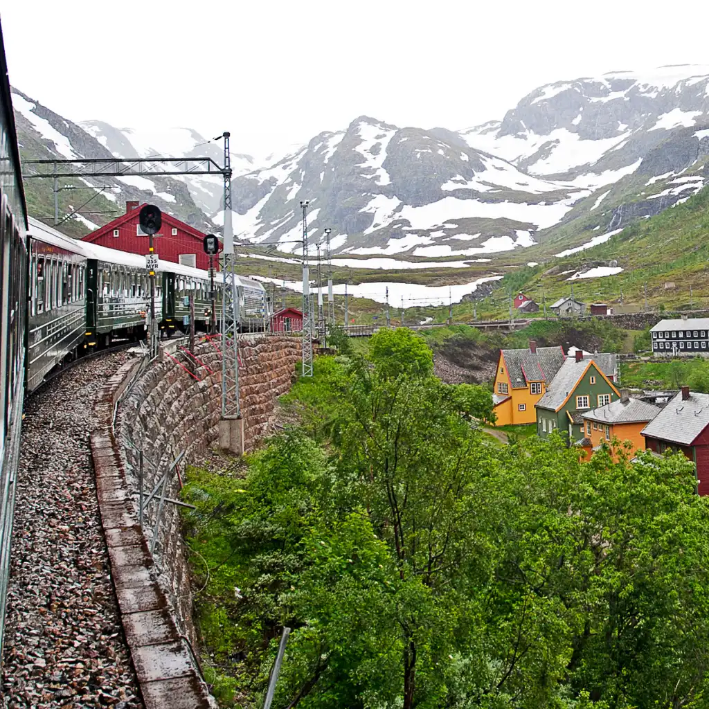 Flam Train, Norway on scenic Flåm Railway amid colorful houses and snowy mountains