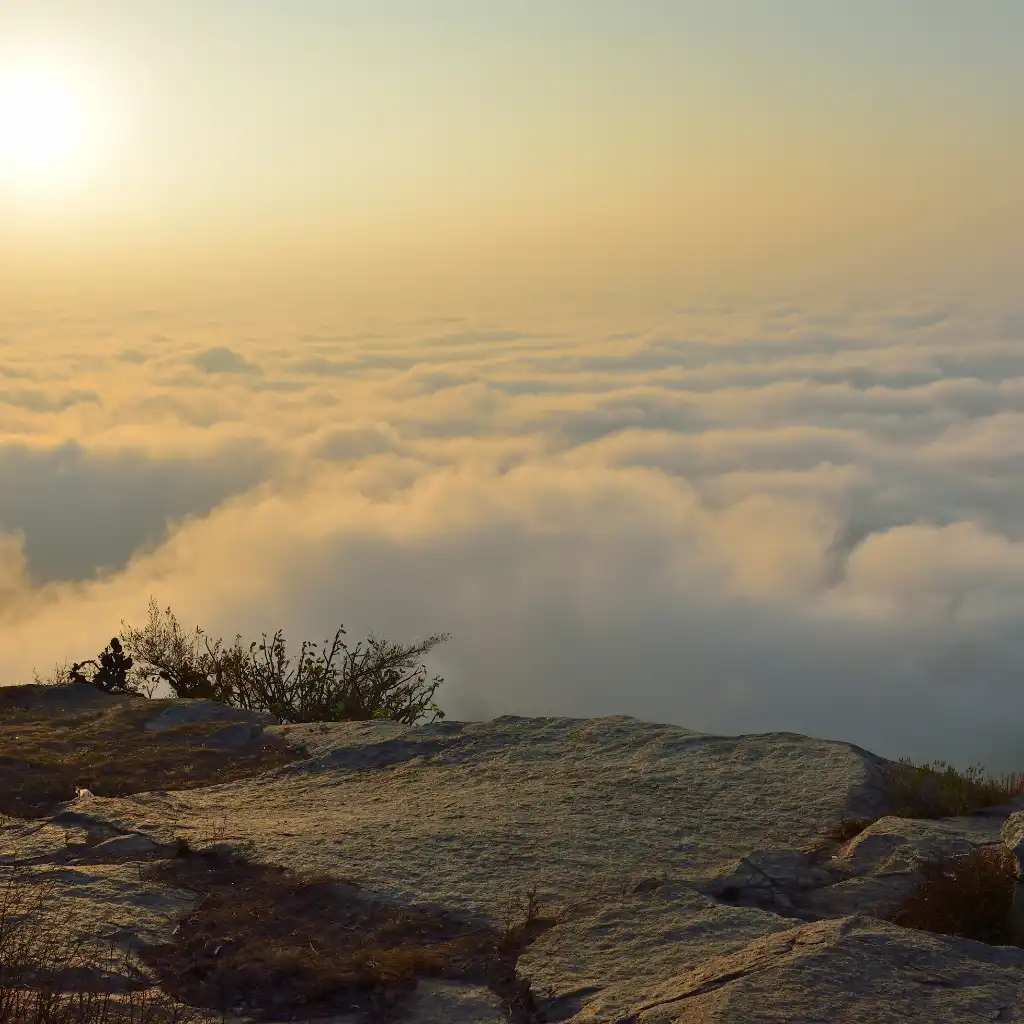 Nandi Hills Bengaluru at dawn with golden sunrise over endless clouds from rocky hilltop