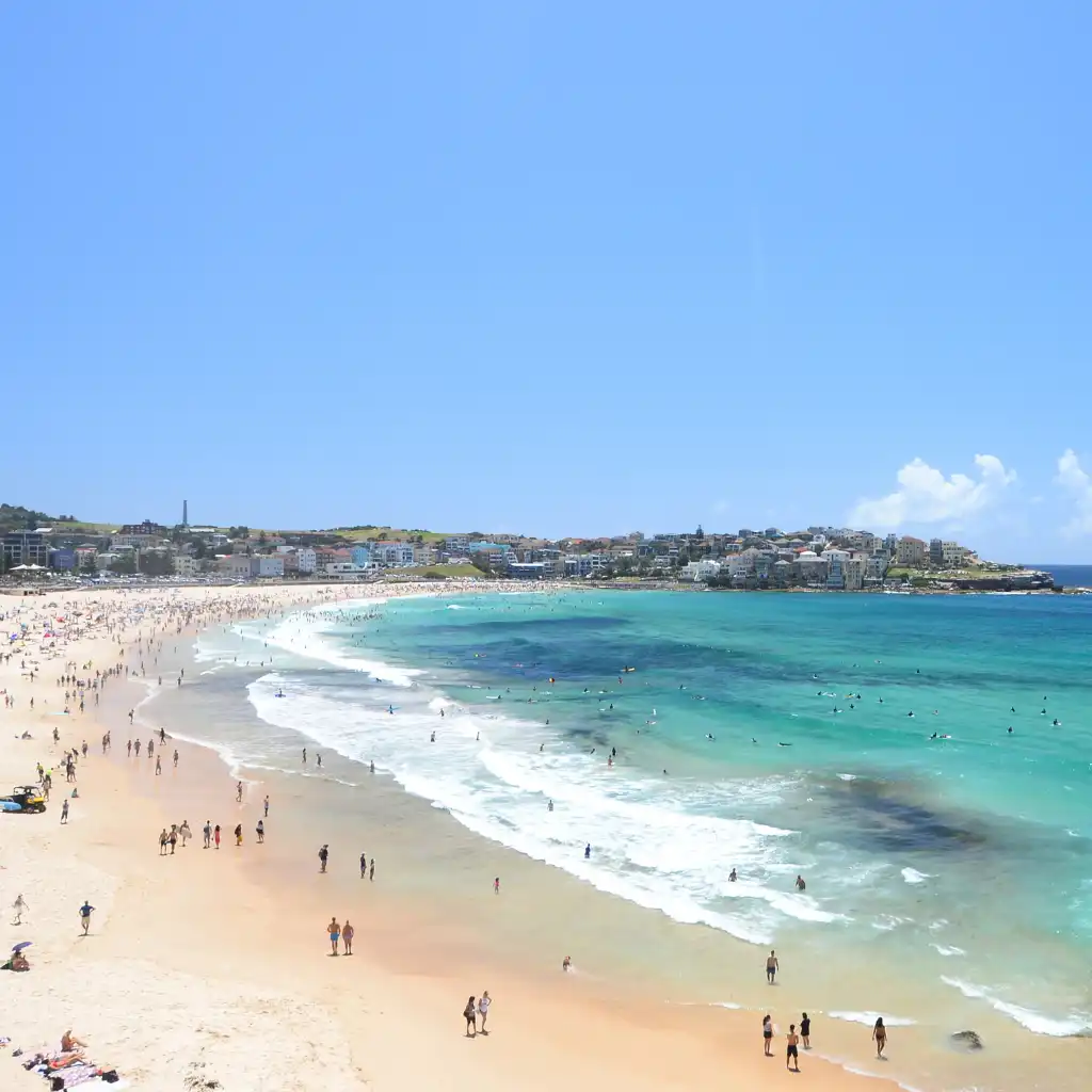 Bondi Beach Sydney crowded with swimmers and sunbathers on golden sand with turquoise waves and city skyline