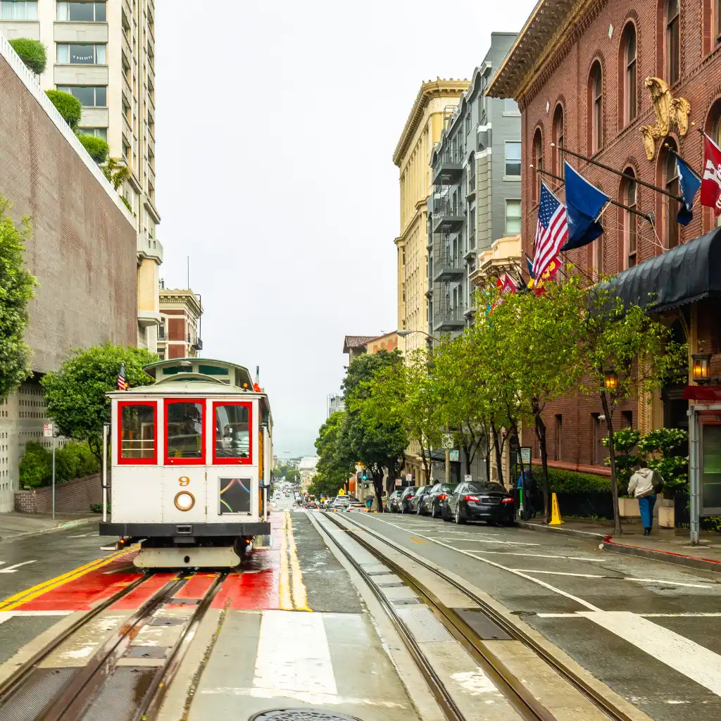 San Francisco cable car on Nob Hill rolling down tracks past city buildings and flags