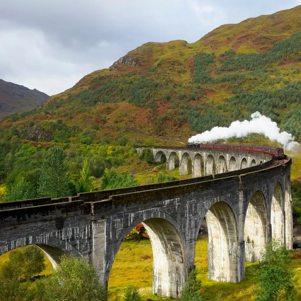 Jacobite steam train curving over viaduct in Scottish Highlands landscape