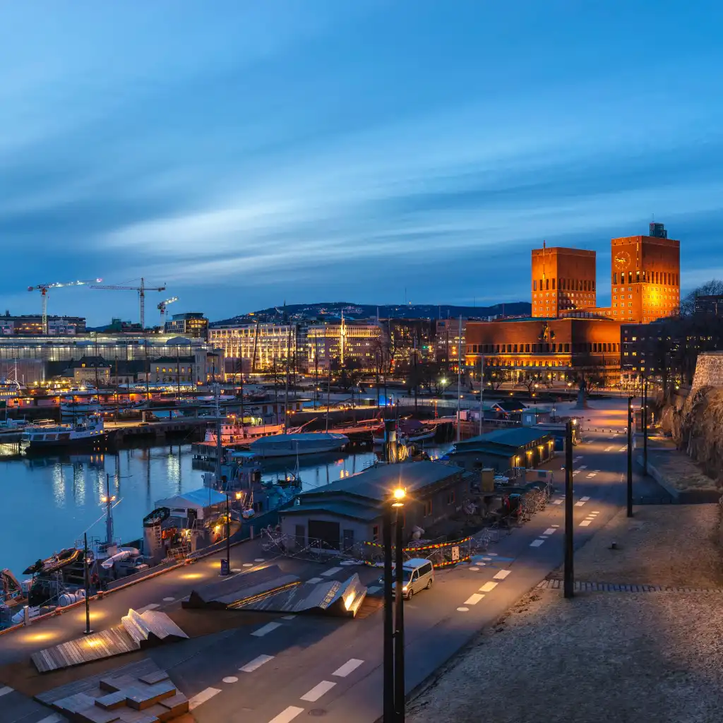 Oslo Central Norway harbor at dusk with glowing modern buildings boats and waterfront promenade
