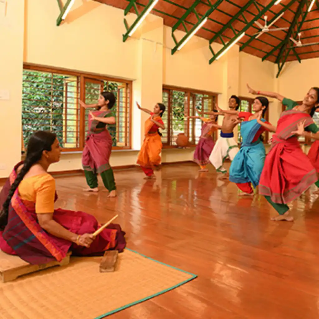 Bharatanatyam class at Kalakshetra with dancers in vibrant costumes performing classical poses under instructor guidance