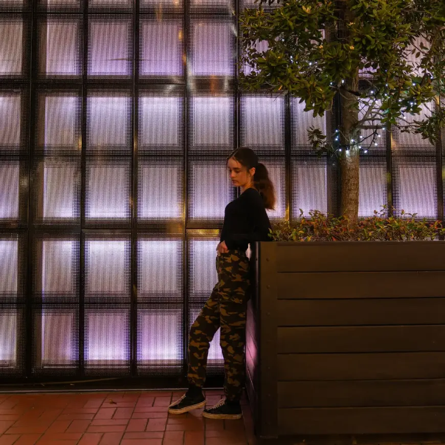 Woman posing in Britomart Area, Auckland by lit wall on waterfront walk at night