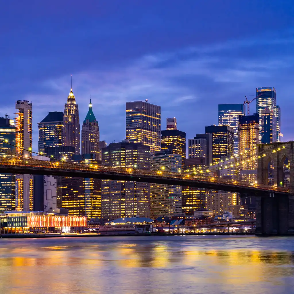 Brooklyn Bridge, New York illuminated at night with glowing Manhattan skyline reflecting on the water