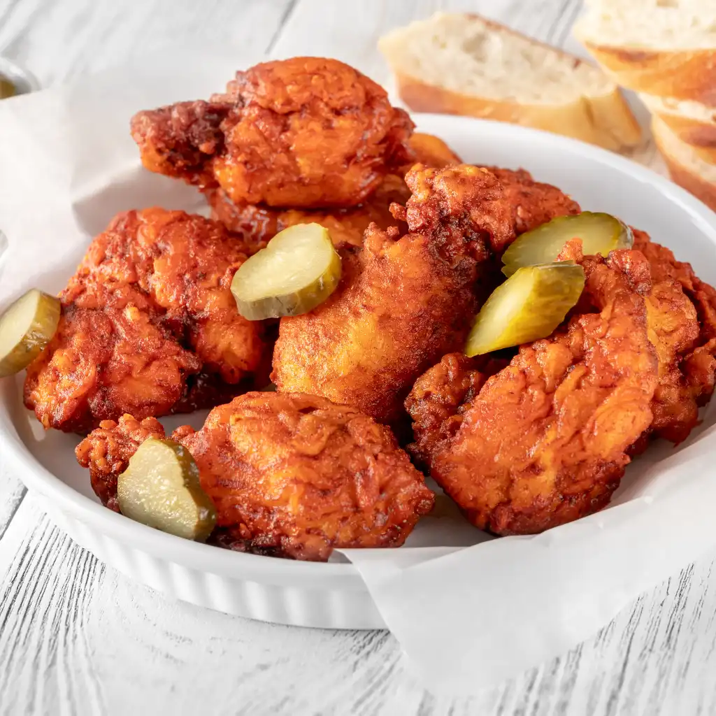 Nashville Hot Chicken with pickles in a white bowl on wooden table