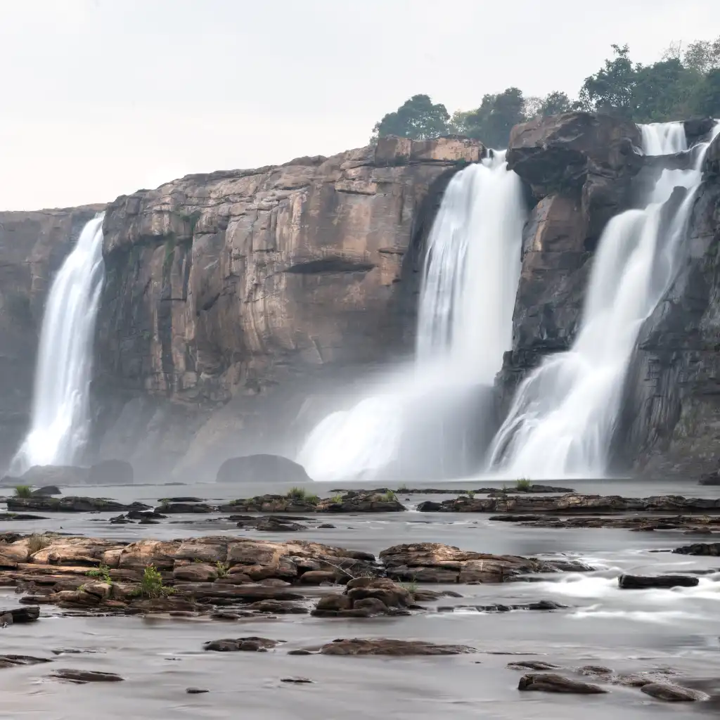 Athirappilly Waterfalls Kerala cascading over rocky cliffs with misty spray and foreground pools