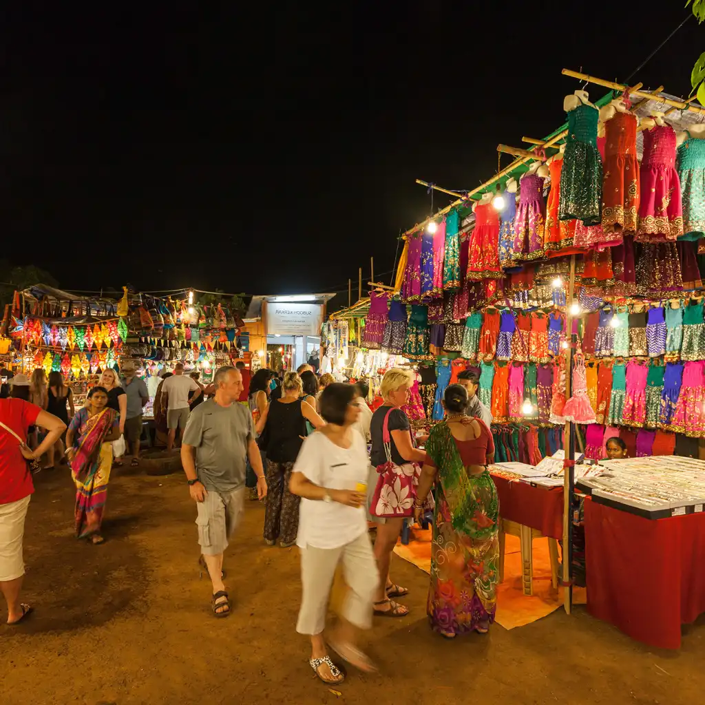 Anjuna Flea Market Goa at night with colorful clothing stalls and evening shoppers browsing