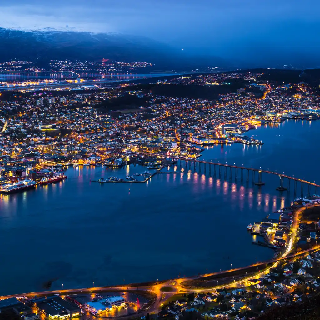 Tromso Norway nightlife with glowing city lights reflecting on the water and bridge at night