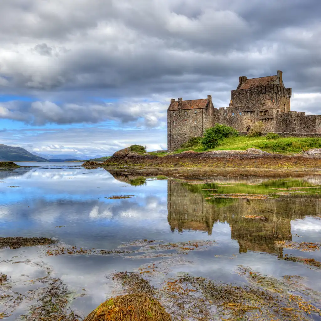 Eilean Donan Castle Scotland reflected in calm loch waters under cloudy skies