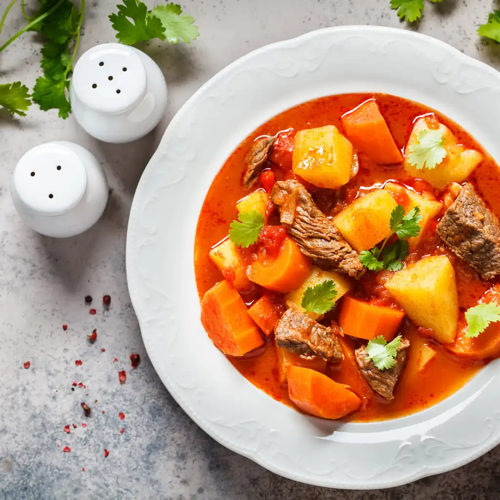 Prague Czech goulash with beef, potatoes and carrots in rich red sauce on white plate