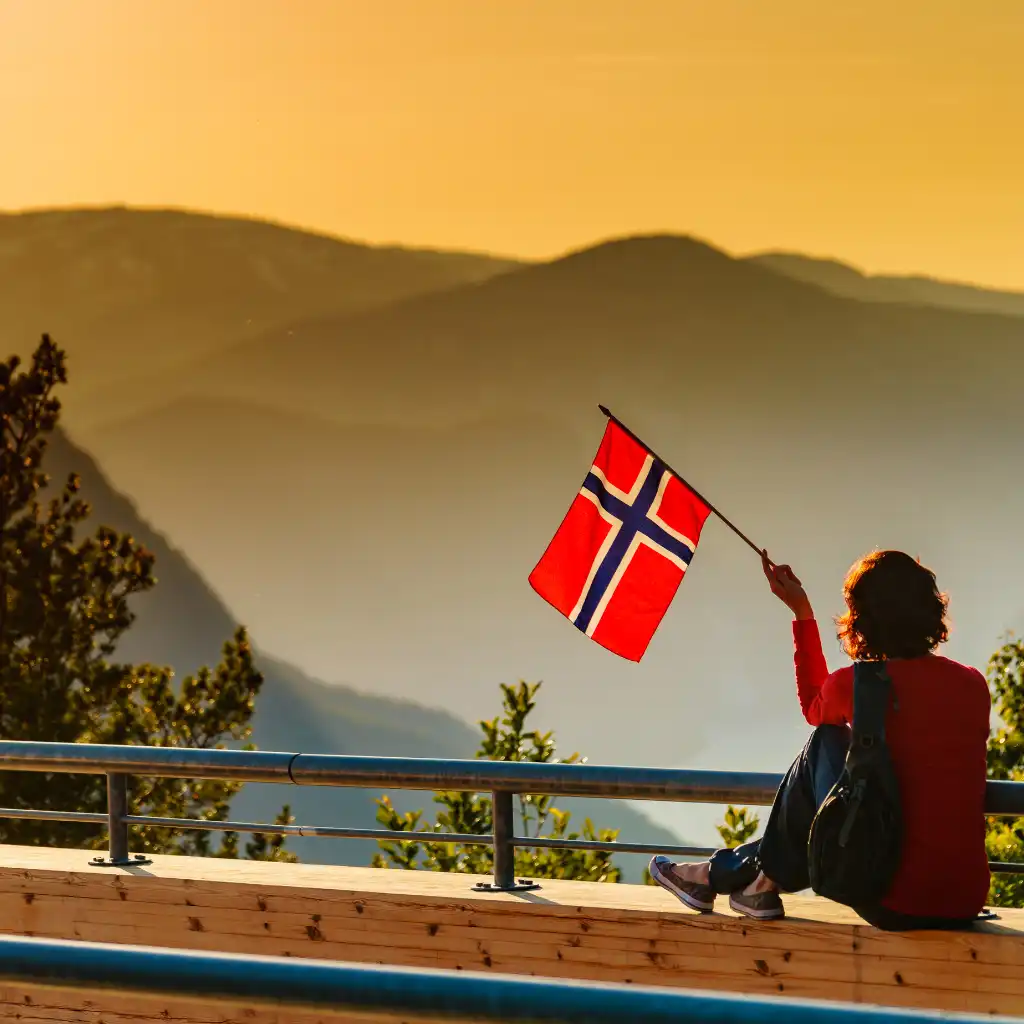 Stegastein Norway: Traveler waves Norwegian flag over misty Aurland mountains at sunset from viewpoint platform
