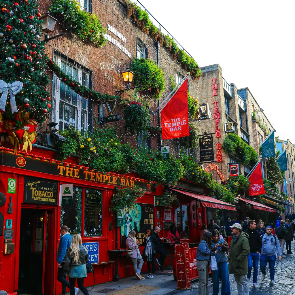 Vibrant Temple Bar pub in Dublin with red facade, crowds and festive decor on cobblestone street