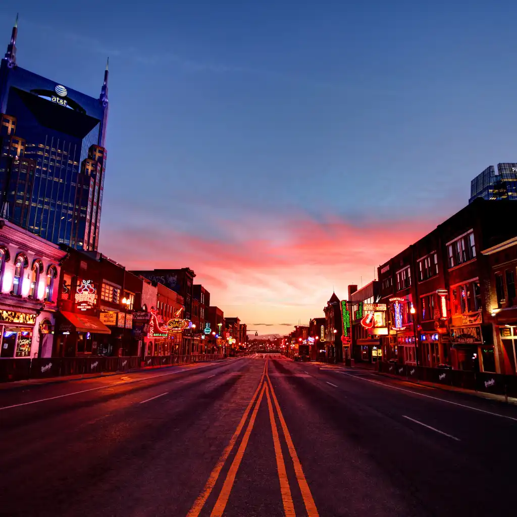 Broadway Nashville at dusk with neon bar signs and AT&T tower along empty street