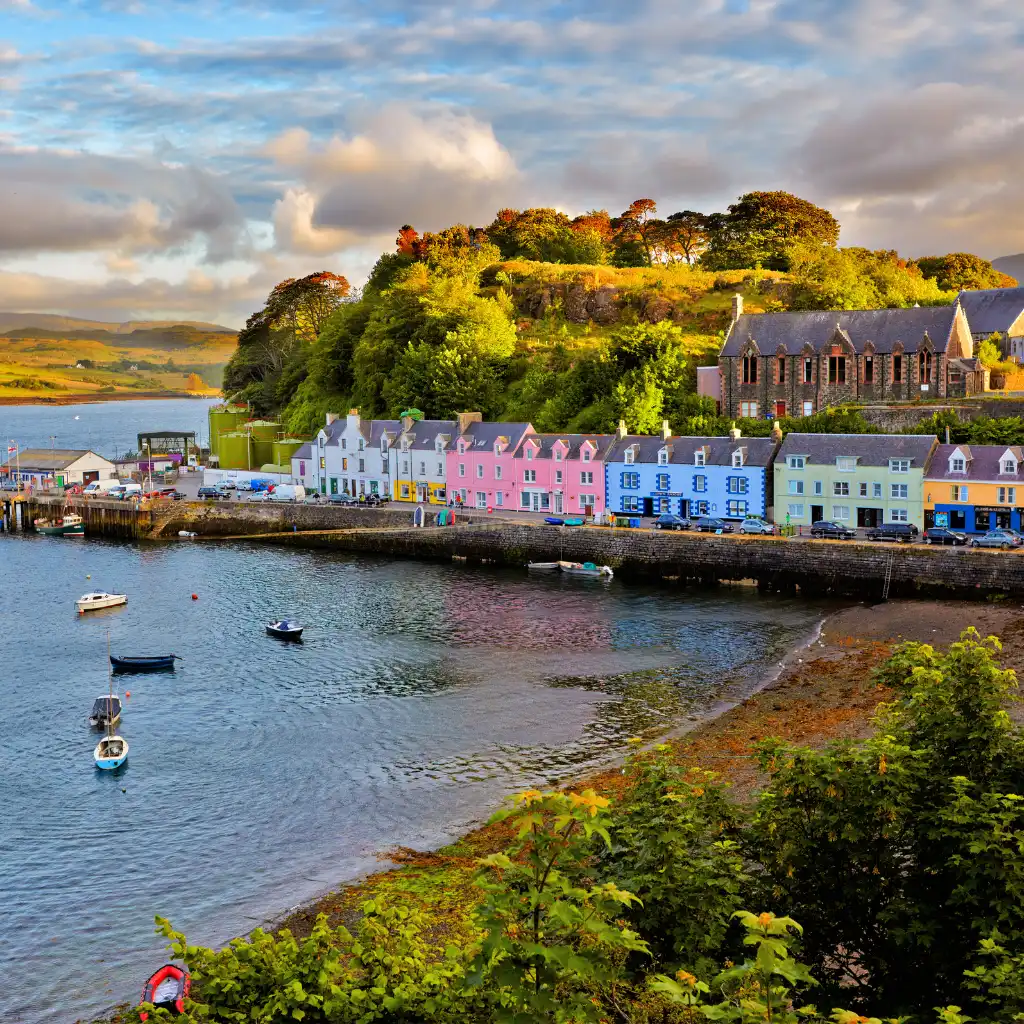 Isle of Skye harbor with colorful houses, boats and green hills at sunset, Scotland