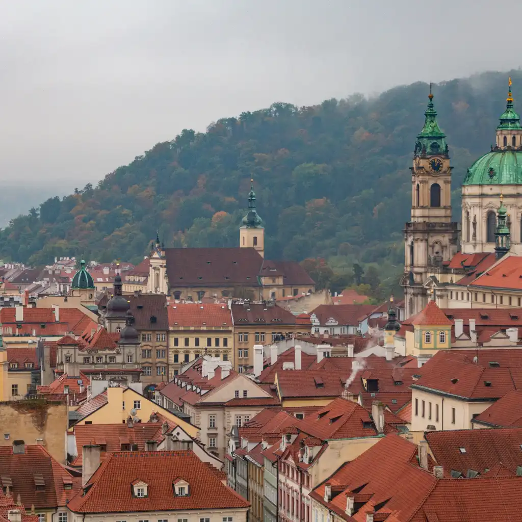 Mala Strana Prague rooftops with red tiles, historic towers and green hill backdrop